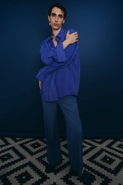Mavi elbiseli yakışıklı bir adam cesur bir duruş sergiliyor, stil ve güven duygusu yayıyor..