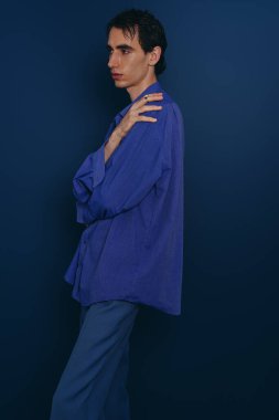 Modaya uygun bir adam kendine güvenen bir poz verir şık mavi bir elbise içinde, çarpıcı mavi bir duvara karşı dizilmiş..