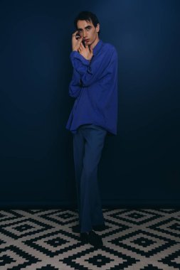 Yakışıklı genç adam çarpıcı mavi kıyafeti ve sanatsal yeteneği ile çağdaş moda sergiliyor..