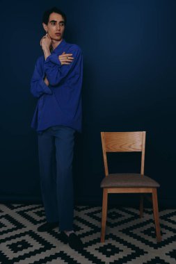 Yakışıklı bir adam boş bir sandalyenin yanında zarif bir şekilde duruyor, şık bir kıyafete güven saçıyor..