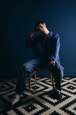 Yakışıklı adam bir sandalyede rahatça oturuyor, rahat ama şık bir atmosfer yaratıyor..