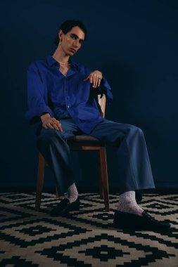 Kendine güveni olan şık bir adam mavi elbiseli bir sandalyede oturur..