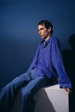 Rahat poz veren yakışıklı bir adam mavi elbiseler giyer ve kendine güveni zengin mavi bir arkaplanda yayılır..