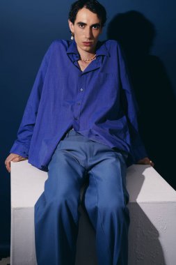 Modaya uygun bir adam dikkat çekici bir mavi arkaplana karşı özgüvenle poz verir, zahmetsiz bir şekilde..