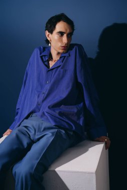 Şık görünümlü, mavi elbiseli yakışıklı bir adam kaideye yaslanmış, etkileyici bir çekiciliği var..