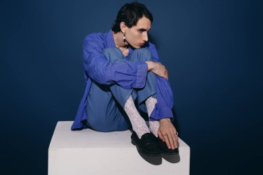 Mavili şık bir adam, eşsiz moda anlayışını yansıtan bir kaidede oturur..