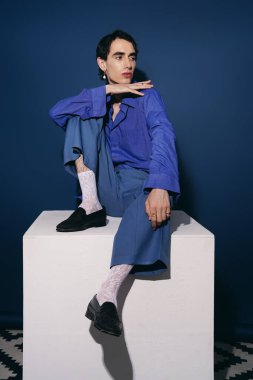 Şık bir adam, yaratıcı bir şekilde tasarlanmış beyaz bir kaidede oturur..