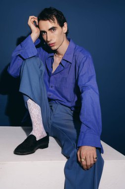 Şık bir adam şık bir kıyafet içinde cesur renklerini sergileyerek düşünceli bir poz verir..