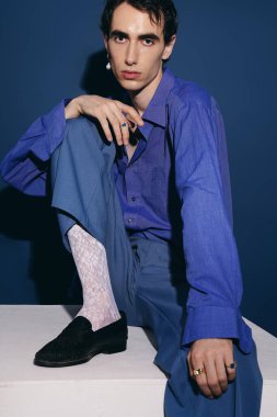 Yakışıklı bir adam sanatsal bir ortamda çarpıcı mavi kıyafetiyle moda anlayışını sergiliyor..