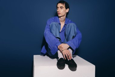 Rahat duruşu olan yakışıklı bir adam, saf mavi arka plana karşı çağdaş modanın altını çiziyor..