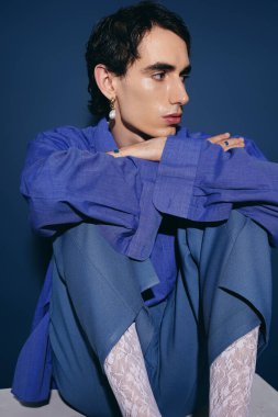 Yakışıklı bir adam bacakları açık, modern moda ve çarpıcı bir görünüm sergiliyor..