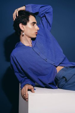 Mavi gömlekli yakışıklı bir adam zarif bir şekilde poz veriyor, modern moda yeteneği sergiliyor..