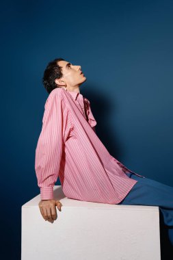 Şık bir adam, kırmızı çizgili gömleğini ve mavi pantolonunu modern bir ortamda sergiliyor..