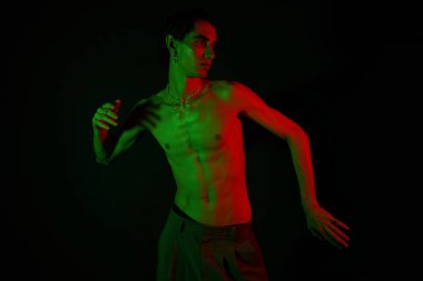 Yakışıklı adam parlak yeşil ve kırmızı ışıkların altında poz veriyor, stili ve özgüveni ile hava atıyor..