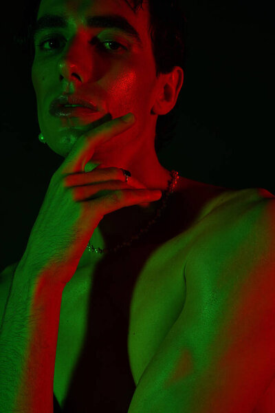 A handsome man showcases his style with a confident pose amid vibrant green and red lighting.