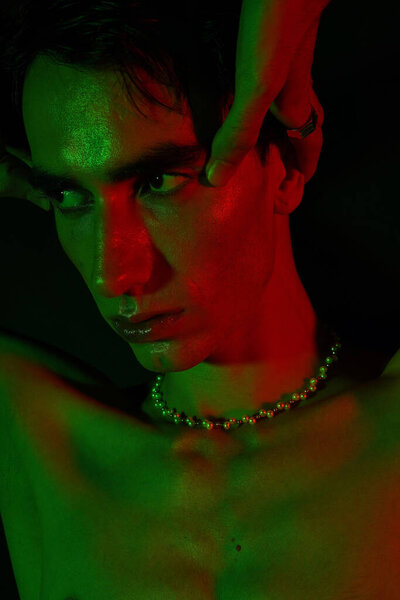 A handsome man poses dramatically under bold green and red lights, showcasing his unique style.