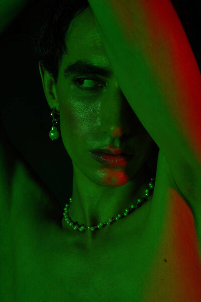 A handsome man radiates confidence in green light, showcasing his bold style and accessories.