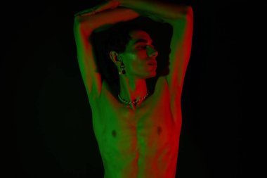 Yakışıklı bir adam, çarpıcı yeşil ve kırmızı ışıklarla aydınlatılmış cesur pozlarla tarzını sergiliyor..