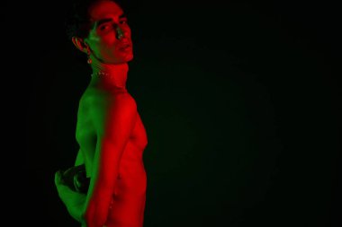 Yakışıklı adam, çarpıcı renkli ışıklandırması olan koyu bir arkaplan karşısında moda tarzını sergiliyor.