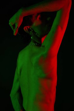 Yakışıklı bir adam kendine güvenerek duruyor, canlı kırmızı ve yeşil ışıklarla aydınlanıyor ve tarzını gösteriyor..