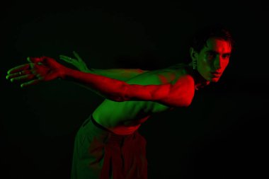 Yakışıklı adam etkileyici bir pozda eşsiz bir stil sergiliyor, canlı kırmızı ve yeşil ışıklarla aydınlatılıyor..