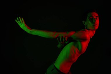 Yakışıklı bir adam çarpıcı bir pozda sanatsal ışıklandırmayla cesur bir moda gösterisi sergiliyor..