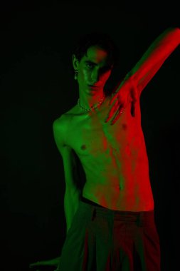 Yakışıklı adam dramatik ışıklandırmayla yaratıcı bir poz veriyor, eşsiz stilini ve kişiliğini sergiliyor..