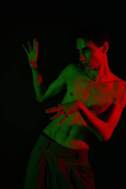 Şık bir adam, canlı kırmızı ve yeşil ışıklarla aydınlatılmış ve dram yaratan eşsiz bir poz sergiliyor..