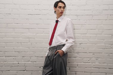 Yakışıklı bir adam dikiliyor, şık elbisesini beyaz bir duvarın yanında sergiliyor..