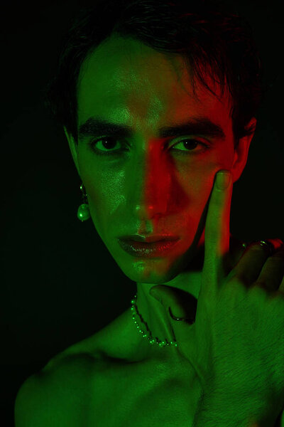 Handsome man poses artistically with striking green and red lighting highlighting his features.