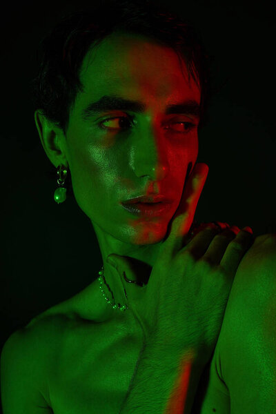 Stylish man poses confidently in striking green and red lighting, highlighting his fashion choices.
