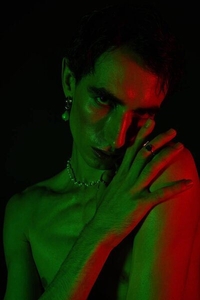 A stylish man poses captivatingly under vibrant green and red lights.