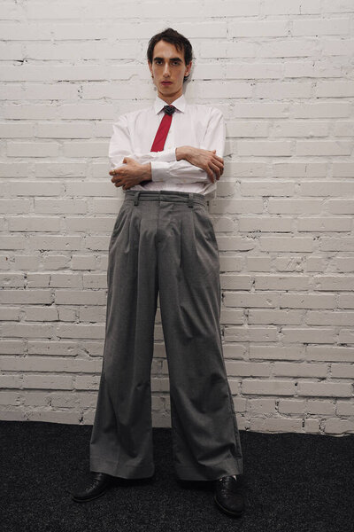 A fashionable man stands with arms crossed, showcasing his stylish attire and confident demeanor.