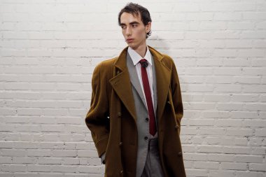 Yakışıklı bir beyefendi, eşsiz moda anlayışını beyaz tuğlalı bir arka planda sergiliyor..