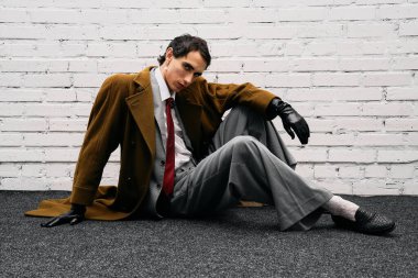 Şık giyinmiş yakışıklı bir adam beyaz bir duvara karşı güven içinde poz verir..