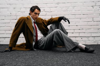 Yakışıklı bir adam zarif moda anlayışını sergileyerek beyaz tuğladan bir duvara yaslanır..