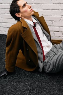 Yakışıklı adam rahat bir şekilde yerde oturuyor, şık bir kıyafet içinde cazibesini sergiliyor..