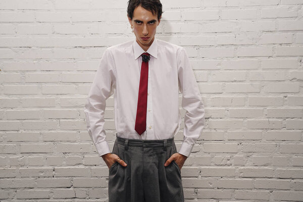 A confident man with striking features showcases modern fashion in a minimalist setting.