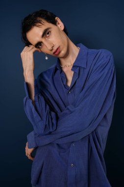Canlı mavi gömlekli yakışıklı bir adam zengin bir arkaplana karşı düşünceli bir şekilde poz verir..
