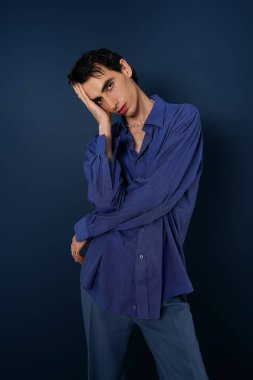 Kusursuz bir tarzı olan yakışıklı bir adam, parlak mavi bir elbiseyle derin bir arkaplanda poz verir..