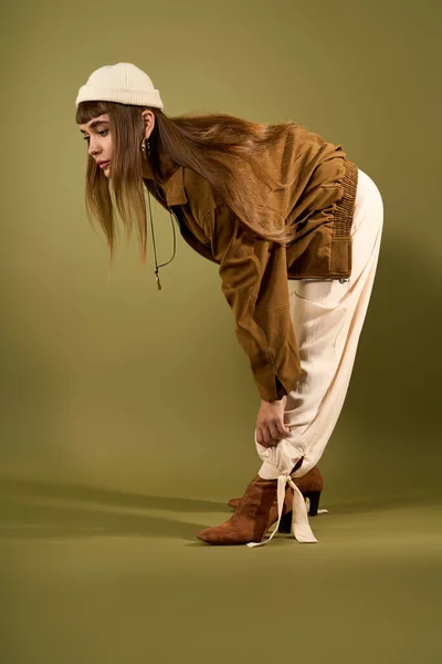 Красива молода жінка налаштовує своє стильне вбрання, позуючи на міцному тлі. — стокове фото