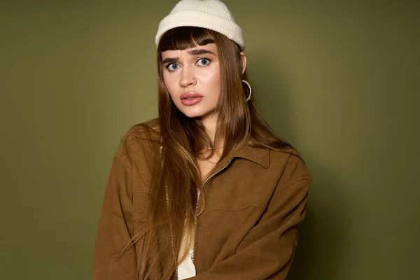 Una mujer joven se para casualmente, alardeando de su estilo único en un gorro y una chaqueta grande. - foto de stock