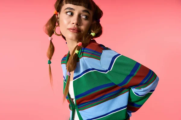 Una giovane donna con le trecce ostenta il suo stile su uno sfondo rosa vibrante, irradiando gioia. — Foto stock