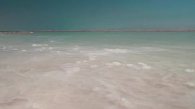 İsrail 'deki ölü denizin mineral tuzu ile mavi gökyüzü ve dağların arka planına karşı HD kalitesinde görüntüler. Güneşte berrak ve şeffaf su parıldar.