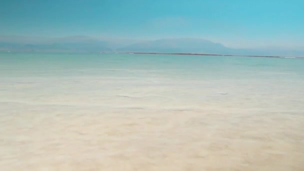 Съемка в HD качестве с минеральной солью Мертвого моря в Израиле на фоне голубого неба и гор. Чистая и прозрачная вода блестит на солнце — стоковое видео
