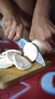 Geleneksel yemek hazırlığı için tahta kesme tahtasıyla kasava kesen bir adamın elleri.