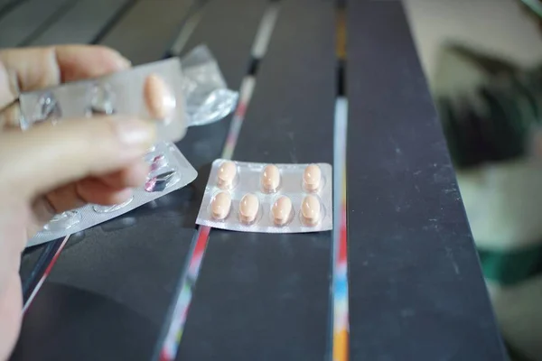 Bir masanın üzerinde duran pembe oval haplardan oluşan su toplayan bir insan eli..