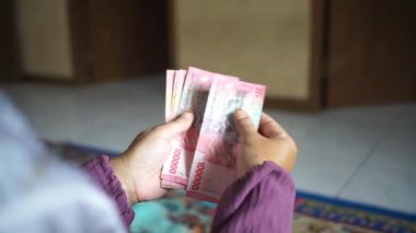 Finansal işlem yaparken kırmızı 100.000 rupiah banknotları sayan eller
