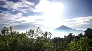 Arka planında görkemli bir dağ olan yeşil doğal manzara ve gökyüzünü kaplayan beyaz bulutlar..