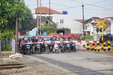 Bandung, Endonezya - 07 Ocak 2026 Demiryolu geçidinde kapalı bariyerler ve bir dizi motosikletle trafik sahnesi.
